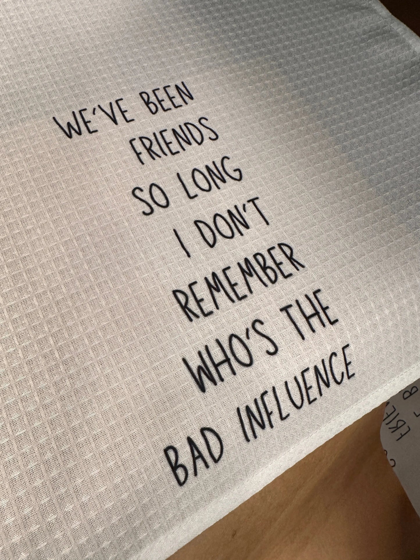 White waffle-weave 18x28 tea towel printed with the phrase “They say it takes a village, but it also takes a vineyard” in black lettering.