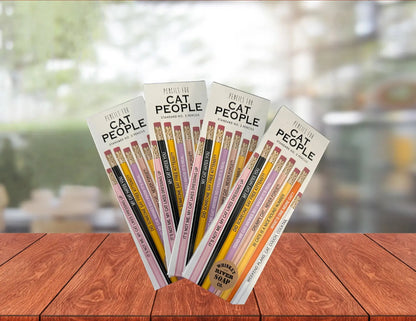 Four packs of “Pencils for Okay Moms” displayed on a wooden table, featuring pink No. 2 pencils printed with funny motherhood sayings.