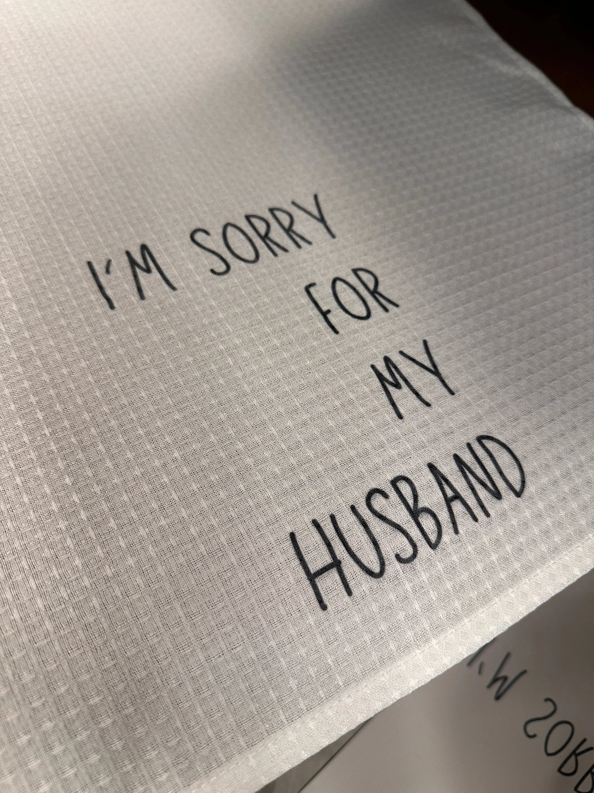 White waffle-weave 18x28 tea towel printed with the phrase “I’m sorry for my husband” in black lettering.
