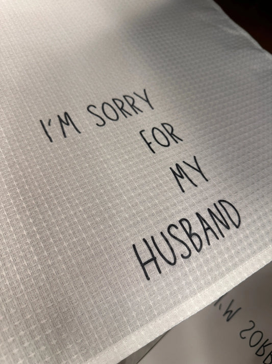 White waffle-weave 18x28 tea towel printed with the phrase “I’m sorry for my husband” in black lettering.