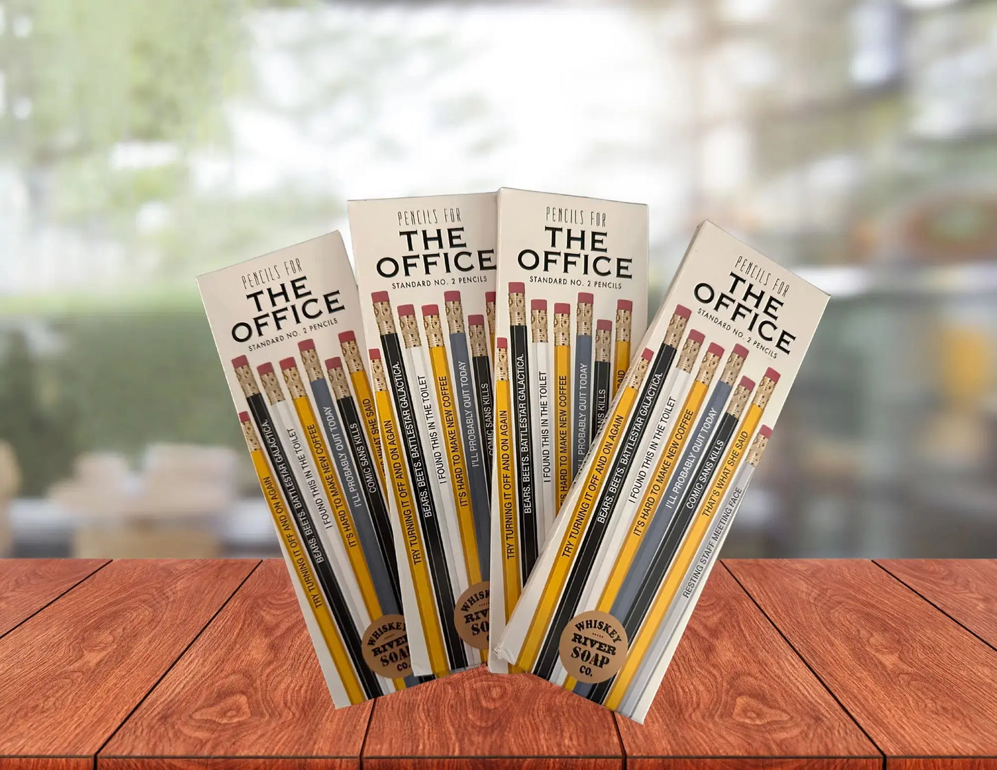 Four packs of “Pencils for The Office” displayed on a wooden table, featuring humorous office-life themed No. 2 pencils.