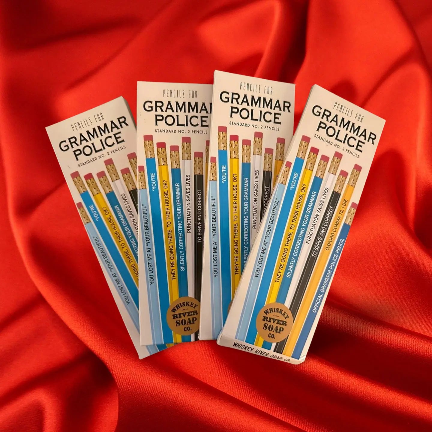 Four packs of “Pencils for Grammar Police” displayed on a wooden table, featuring blue and yellow No. 2 pencils printed with funny grammar quotes.