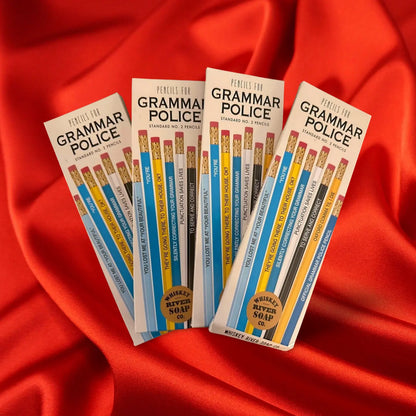 Four packs of “Pencils for Grammar Police” displayed on a wooden table, featuring blue and yellow No. 2 pencils printed with funny grammar quotes.