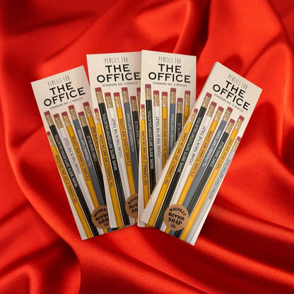 Four packs of “Pencils for The Office” displayed on a wooden table, featuring humorous office-life themed No. 2 pencils.